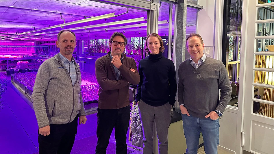 Four people stand in front of an indoor greenhouse with purple lights.