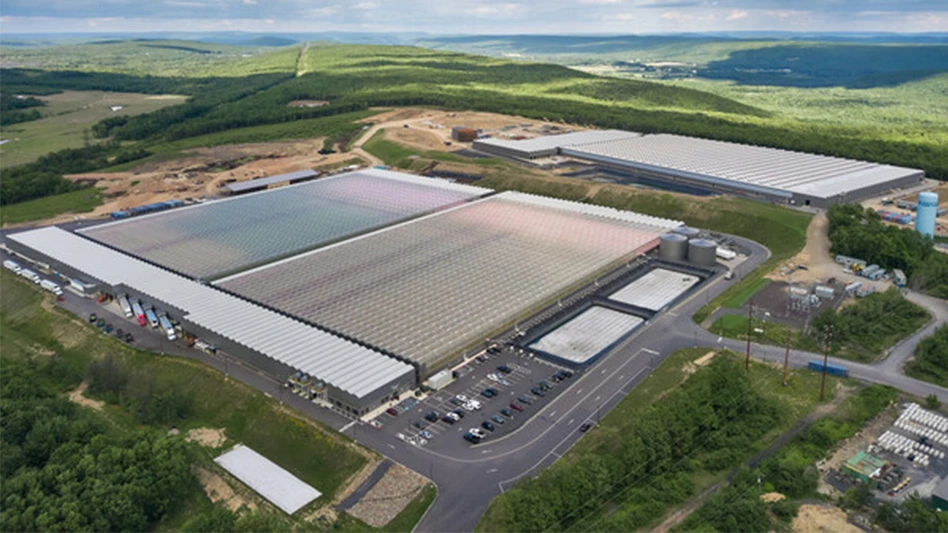 Overhead view of a large greenhouse surrounded by rolling green hills.