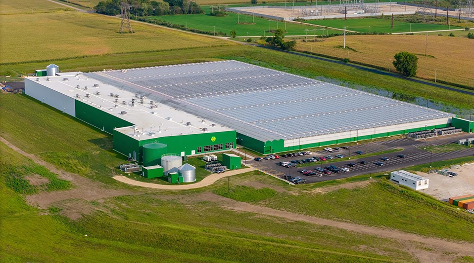 An overview photo of a large, square, green and white building, surrounded by green fields.