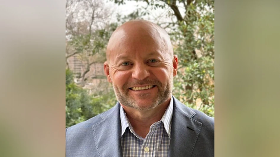 A photo of a smiling bald man wearing a blue and white plaid button-up shirt and blue suit jacket.