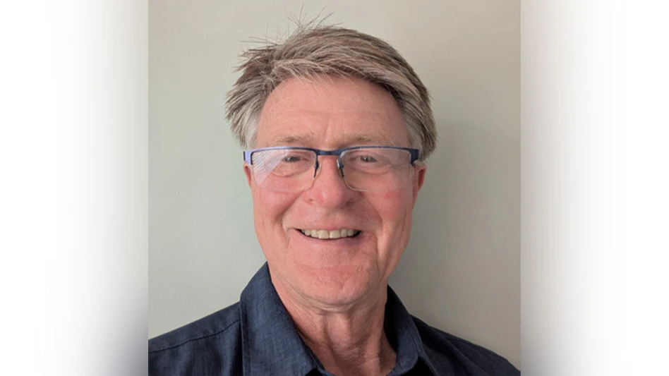 A selfie photo of a smiling man with short gray hair and wearing glasses and a dark blue button-up shirt.