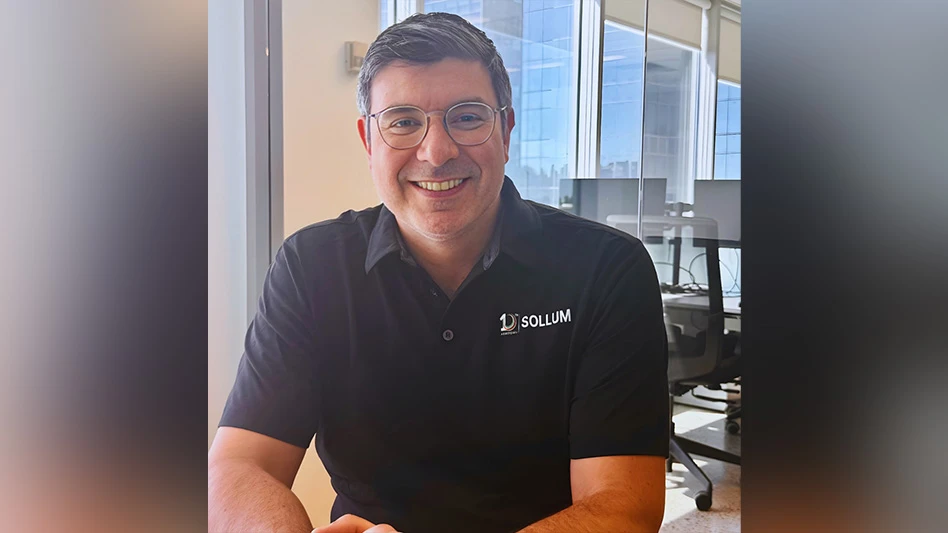 A smiling man with short brown hair wearing glasses and a black polo shirt.