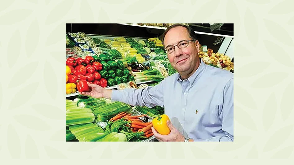 Craig Carlson reaching his hand out over produce in a grocery store.