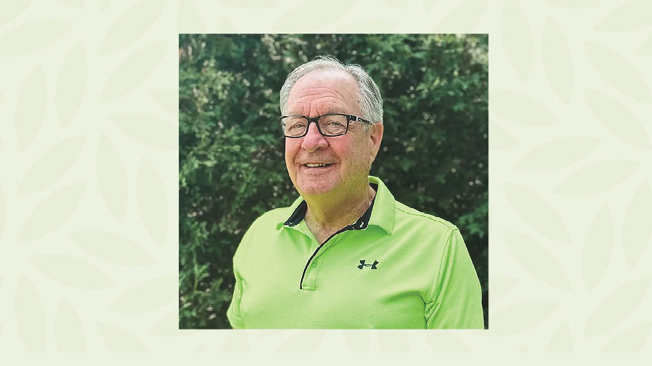 A man in a neon green shirt standing in front of leafy foliage.