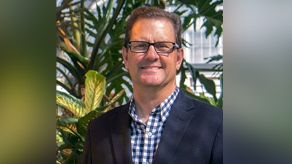 A man wearing a navy blue suit standing in front of tropical plants.