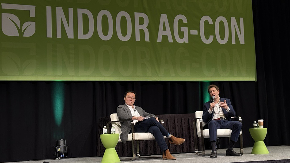 Two men sitting on a stage with a green banner reading Indoor Ag-Con behind them..