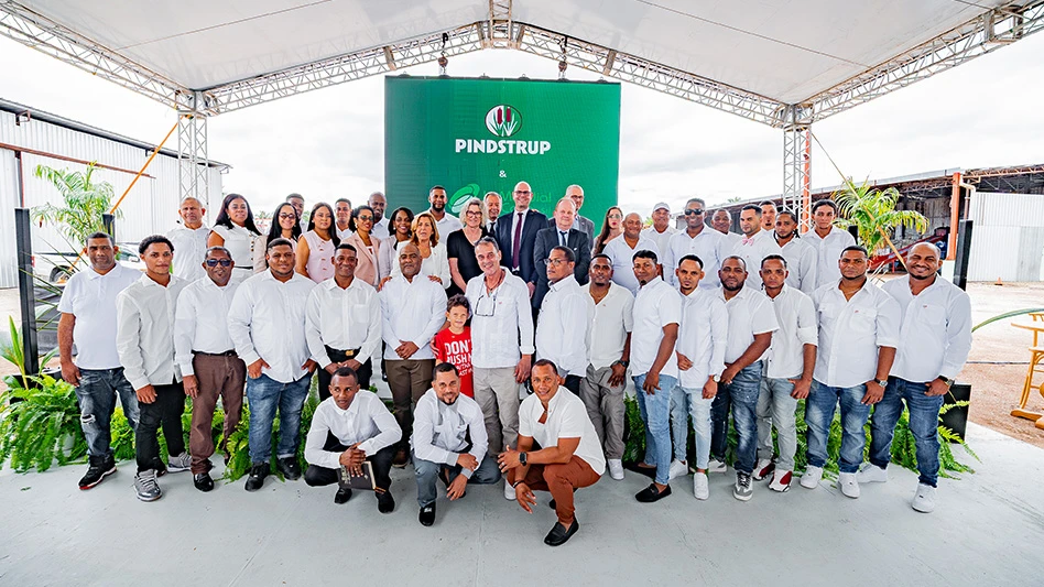 A crowd of smiling people under a white tent in front of a green sign.