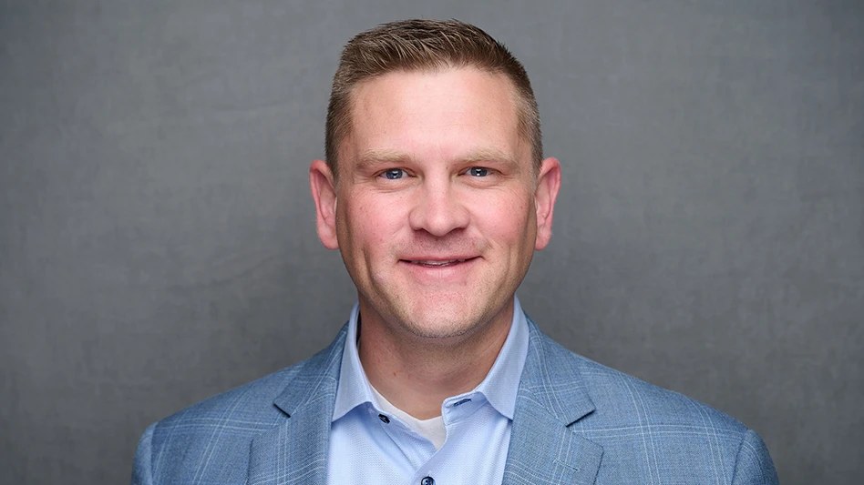 A headshot photo of a smiling man with short brown hair and wearing a blue suit jacket and light blue shirt.